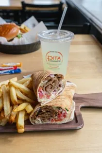 A gyro wrap cut in half and served with fries and a drink at Pita Corner
